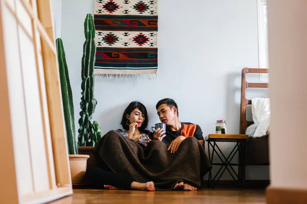 Genç bir Malay çift yatmak ve evlerinde sıcak bir içecek paylaşın. Onlar sarılır up ve birbirleriyle konuşmak gibi zemin ve rahat oturan.