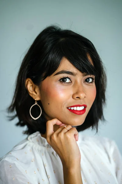 Portrait of a young, tall and slim Malay woman in a white shirt and black pants against a white background