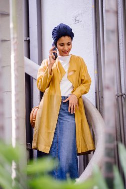 Genç ve çekici Malay Müslüman kadın basamaklardan iniyor ve gün boyunca onun smartphone üzerinde konuşuyor