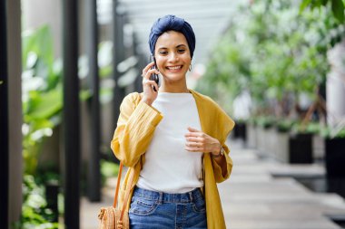 Genç ve çekici Malay Müslüman kadın basamaklardan iniyor ve gün boyunca onun smartphone üzerinde konuşuyor