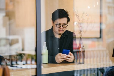 Bir Çinli bir polo ve bir kafede oturan ve smartphone kullanarak ceket portresi