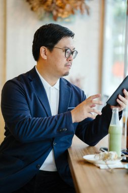 Bir Çinli bir polo ve bir kafede oturan ve gün boyunca onun tablet üzerinde çalışan ceket portresi. 