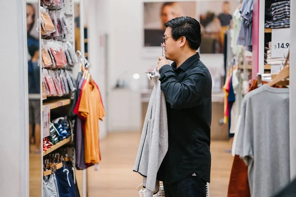 A middle-aged Chinese man is shopping for clothing in a fast fashion store.