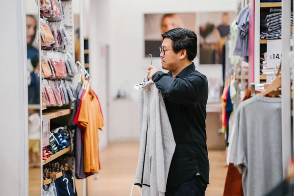 A middle-aged Chinese man is shopping for clothing in a fast fashion store.