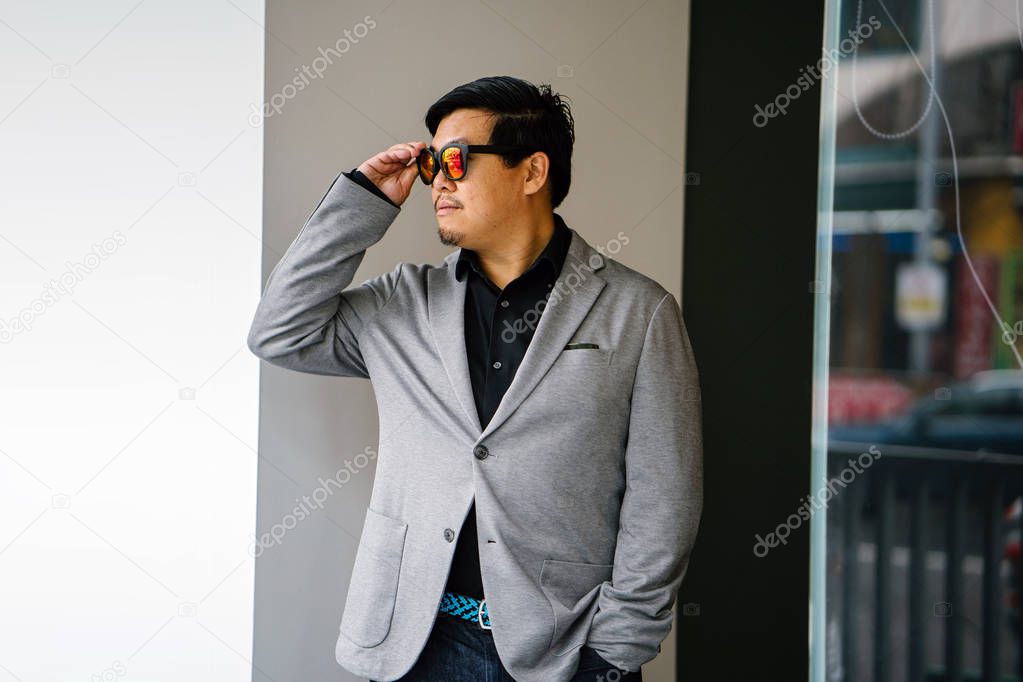 portrait of a Chinese Asian man in a grey suit, black shirt and sunglasses (smart casual). He is confident, cool and handsome in his smart casual outfit 