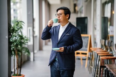 Bir eğitimli, orta yaşlı Çinli Asyalı portresi dostum iş casual ve gözlük. O holding ve çay bir zarif Kupası ve fincan tabağı gün boyunca şehrin içme.