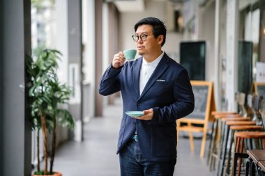 Bir eğitimli, orta yaşlı Çinli Asyalı portresi dostum iş casual ve gözlük. O holding ve çay bir zarif Kupası ve fincan tabağı gün boyunca şehrin içme.