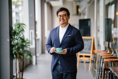 Bir eğitimli, orta yaşlı Çinli Asyalı portresi dostum iş casual ve gözlük. O holding ve çay bir zarif Kupası ve fincan tabağı gün boyunca şehrin içme.