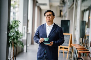 Bir eğitimli, orta yaşlı Çinli Asyalı portresi dostum iş casual ve gözlük. O holding ve çay bir zarif Kupası ve fincan tabağı gün boyunca şehrin içme.