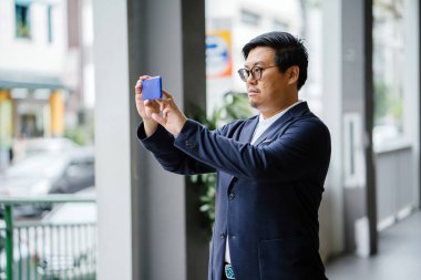 Bir fotoğraf gün boyunca onun Smartphone'da alarak kendine güvenen orta yaşlı bir Çinli Asya adam portresi. Akıllı rahat (polo, ceket ve kot pantolon giymiş).