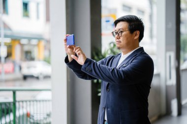 Bir fotoğraf gün boyunca onun Smartphone'da alarak kendine güvenen orta yaşlı bir Çinli Asya adam portresi. Akıllı rahat (polo, ceket ve kot pantolon giymiş).