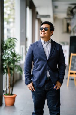 Orta yaşlı Çinli Asyalı portresi (Singapurlu) şehrin smart casual ayakta dostum. O iyi giyimli ve bakımlı bir donanma takım, güneş gözlüğü ile oxford düğme aşağı gömlek..