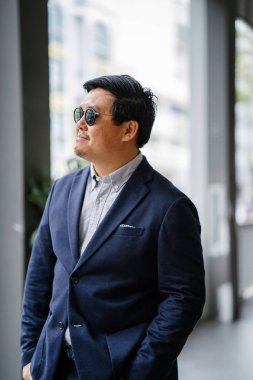 Orta yaşlı Çinli Asyalı portresi (Singapurlu) şehrin smart casual ayakta dostum. O iyi giyimli ve bakımlı bir donanma takım, güneş gözlüğü ile oxford düğme aşağı gömlek..