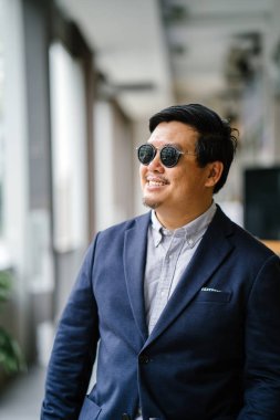 Orta yaşlı Çinli Asyalı portresi (Singapurlu) şehrin smart casual ayakta dostum. O iyi giyimli ve bakımlı bir donanma takım, güneş gözlüğü ile oxford düğme aşağı gömlek..