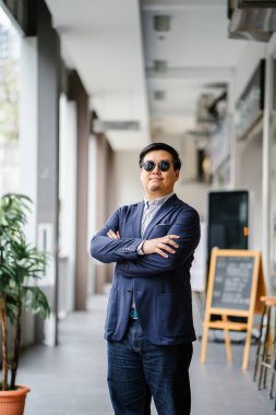 Orta yaşlı Çinli Asyalı portresi (Singapurlu) şehrin smart casual ayakta dostum. O iyi giyimli ve bakımlı bir donanma takım, güneş gözlüğü ile oxford düğme aşağı gömlek..