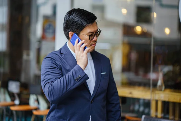 Portrait of a middle-aged Chinese Asian man in a casual suit. He is talking on his phone