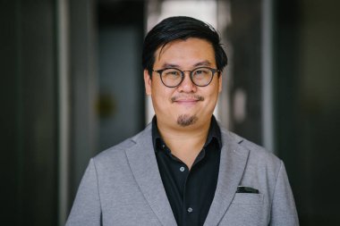 Bir eğitimli ve orta yaşlı Çinli Asyalı (Singapurlu) portresi siyah gömlek ve gri takım dostum. Kameraya gazes gibi gülümsüyor.