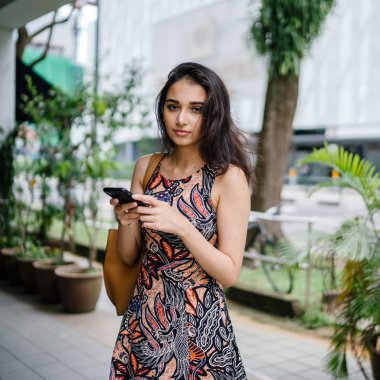 ayakta ve gün boyunca Asya'da bir şehirde kentsel bir sokakta onun smartphone kullanarak Genç Hintli Asyalı kadın