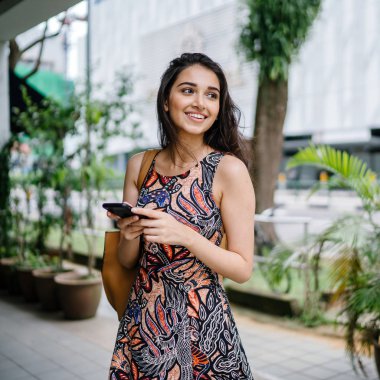 ayakta ve gün boyunca Asya'da bir şehirde kentsel bir sokakta onun smartphone kullanarak Genç Hintli Asyalı kadın