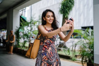 Genç, güzel ve zarif Punjabi Hint Asyalı kadın kendini bir selfie onun smartphone ile yoğun bir cadde üzerinde gün boyunca alır