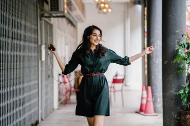 Kulaklıkla müzik dinlerken dans eden genç, çekici ve güzel bir Hint Asyalı kızın portresi. O, akıllı telefonunda müzik yayınlıyor.