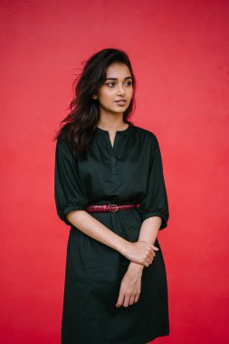 Kızıl stüdyo arka planına karşı güzel, genç ve çekici bir Hintli kadının stüdyo portresi. Zarif giyinmiş.