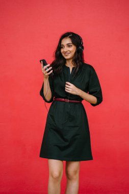 Genç, çekici ve güzel Hint Asyalı kız kulaklıkla müzik dinlerken dans ediyor. O, akıllı telefonunda müzik yayınlıyor.