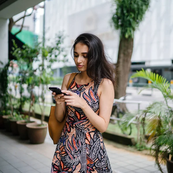 年轻的印度亚裔妇女站在亚洲一个城市的城市街道上使用智能手机 — 图库照片