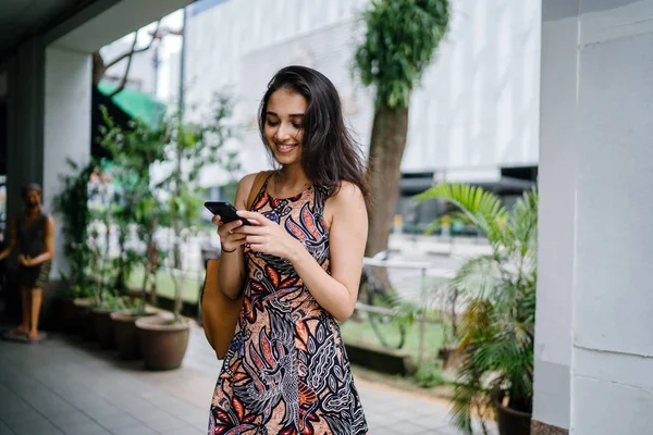 年轻的印度亚裔妇女站在亚洲一个城市的城市街道上使用智能手机 — 图库照片