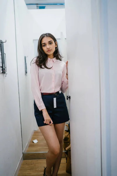 Portrait of a young and beautiful Indian Asian woman trying out new clothing in a fitting room in a fashion shop in a mall.