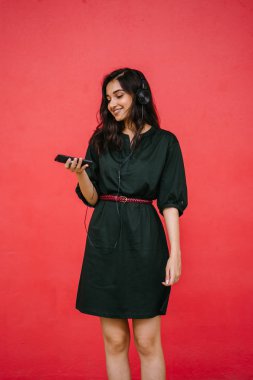 Genç, çekici ve güzel Hint Asyalı kız kulaklıkla müzik dinlerken dans ediyor. O, akıllı telefonunda müzik yayınlıyor.