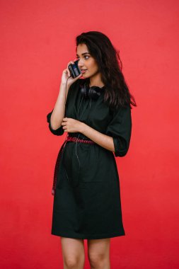 Yeşil elbiseli, kırmızı kemerli, güzel, genç ve çekici bir Hintli kadının stüdyo portresi. Akıllı telefonunu kullanıyor..