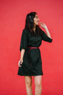 Genç, çekici ve güzel Hint Asyalı kız kulaklıkla müzik dinlerken dans ediyor. O, akıllı telefonunda müzik yayınlıyor.