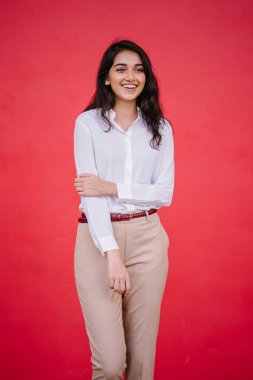 Kızıl stüdyo arka planına karşı güzel, genç ve çekici bir Hintli kadının stüdyo portresi. Zarif giyinmiş.