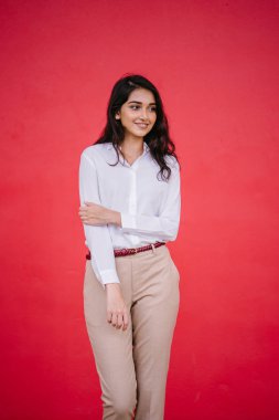 Kızıl stüdyo arka planına karşı güzel, genç ve çekici bir Hintli kadının stüdyo portresi. Zarif giyinmiş.