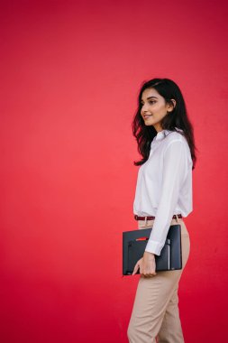 Kızıl stüdyo arka planına karşı güzel, genç ve çekici bir Hintli kadının stüdyo portresi. Zarif giyinmiş.