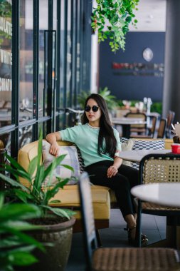 Genç ve çekici Çinli Asyalı bir kadının portresi uzanarak ve bir hafta sonu gün boyunca bir kafede rahatlatıcı. Nane yeşili bir kazak giyiyor.