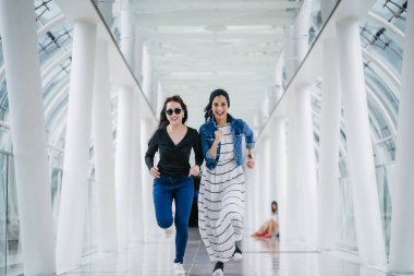 İki farklı arkadaş, iyi aydınlatılmış beyaz fütüristik bir üstgeçit köprüsünden kameraya doğru koşuyorlar. Biri Müslüman bir Orta Doğulu kadın, diğeri de Çinli..