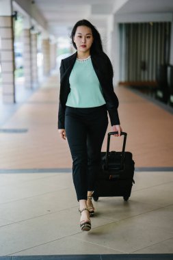 Genç bir Asyalı kadın bavulunu çekiyor. O çekici, zarif ve şık giyinmiş