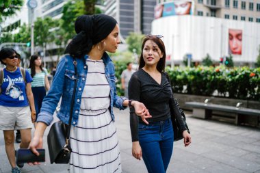 İki arkadaş, Orchard Road, Singapur, Asya 'da aydınlık bir yaz gününde mutlu bir şekilde yürüyüp konuşurlar. Biri Müslüman Malezyalı, diğeri Çinli bir kadın.. 