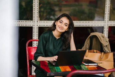 genç üniversite öğrencisi (Hint Asyalı kadın) eğitim ve gün boyunca dizüstü bilgisayar bir masa başında çalışma