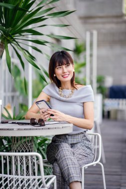 Çekici, kendine güvenen ve başarılı bir Çinli Asyalı kadının portresi. Akıllı telefonunu tutuyor. 