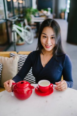 Bir açık havada açık havada oturan ve kırmızı bir çay seti çay sıcak bir fincan zevk genç, çekici, zarif ve güzel Asyalı kadın Portresi. 