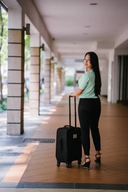 Genç bir Asyalı kadın bavulunu çekiyor. O çekici, zarif ve şık giyinmiş