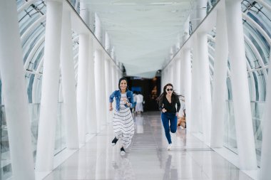 İki farklı arkadaş, iyi aydınlatılmış beyaz fütüristik bir üstgeçit köprüsünden kameraya doğru koşuyorlar. Biri Müslüman bir Orta Doğulu kadın, diğeri de Çinli..