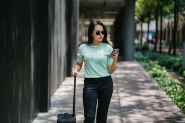 Genç bir Asyalı kadın bavulunu çekiyor. O çekici, zarif ve şık giyinmiş