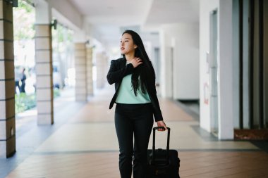 Genç bir Asyalı kadın bavulunu çekiyor. O çekici, zarif ve şık giyinmiş