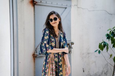 uzun boylu, zarif ve güzel Hint Asyalı kadın yaz elbise ve güneş gözlüğü gülümsüyor o pozlar gün boyunca bir arka sokakta bir sokakta olarak içinde