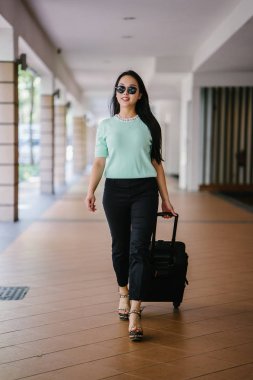 Genç bir Asyalı kadın bavulunu çekiyor. O çekici, zarif ve şık giyinmiş