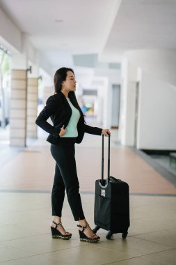 Genç bir Asyalı kadın bavulunu çekiyor. O çekici, zarif ve şık giyinmiş